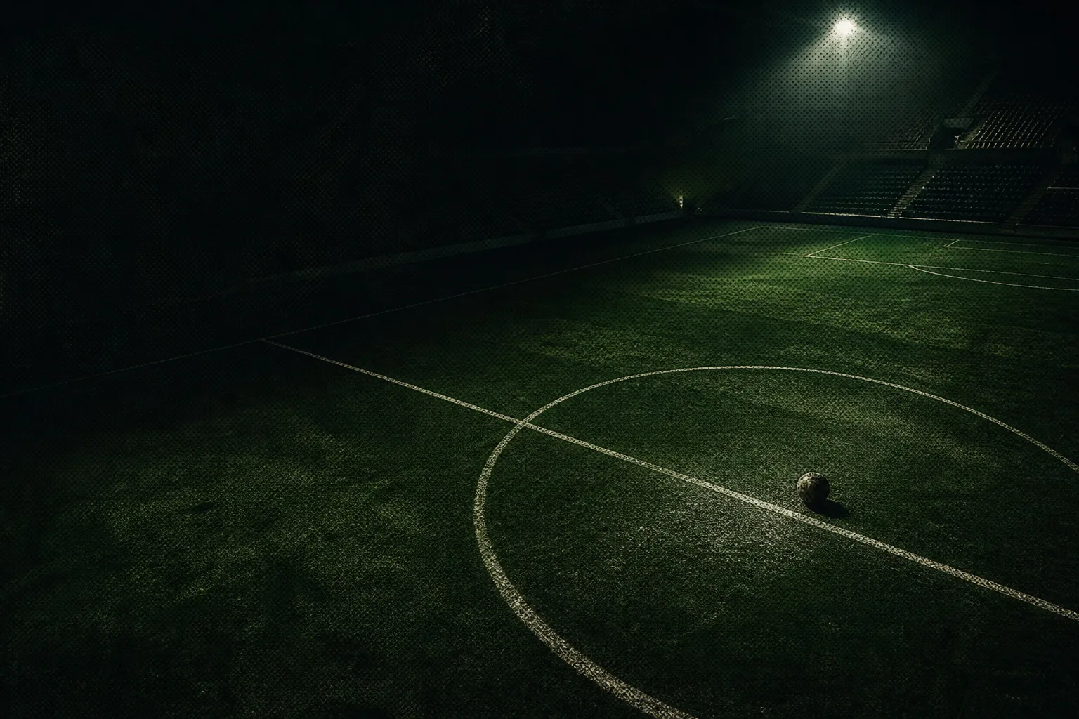 Cancha de fútbol de noche con una pelota junto al círculo central